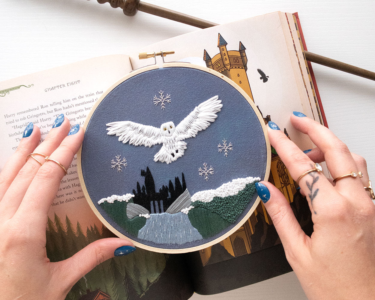 Magical Owl Embroidery Kit finished on an open book with a wand held by hands