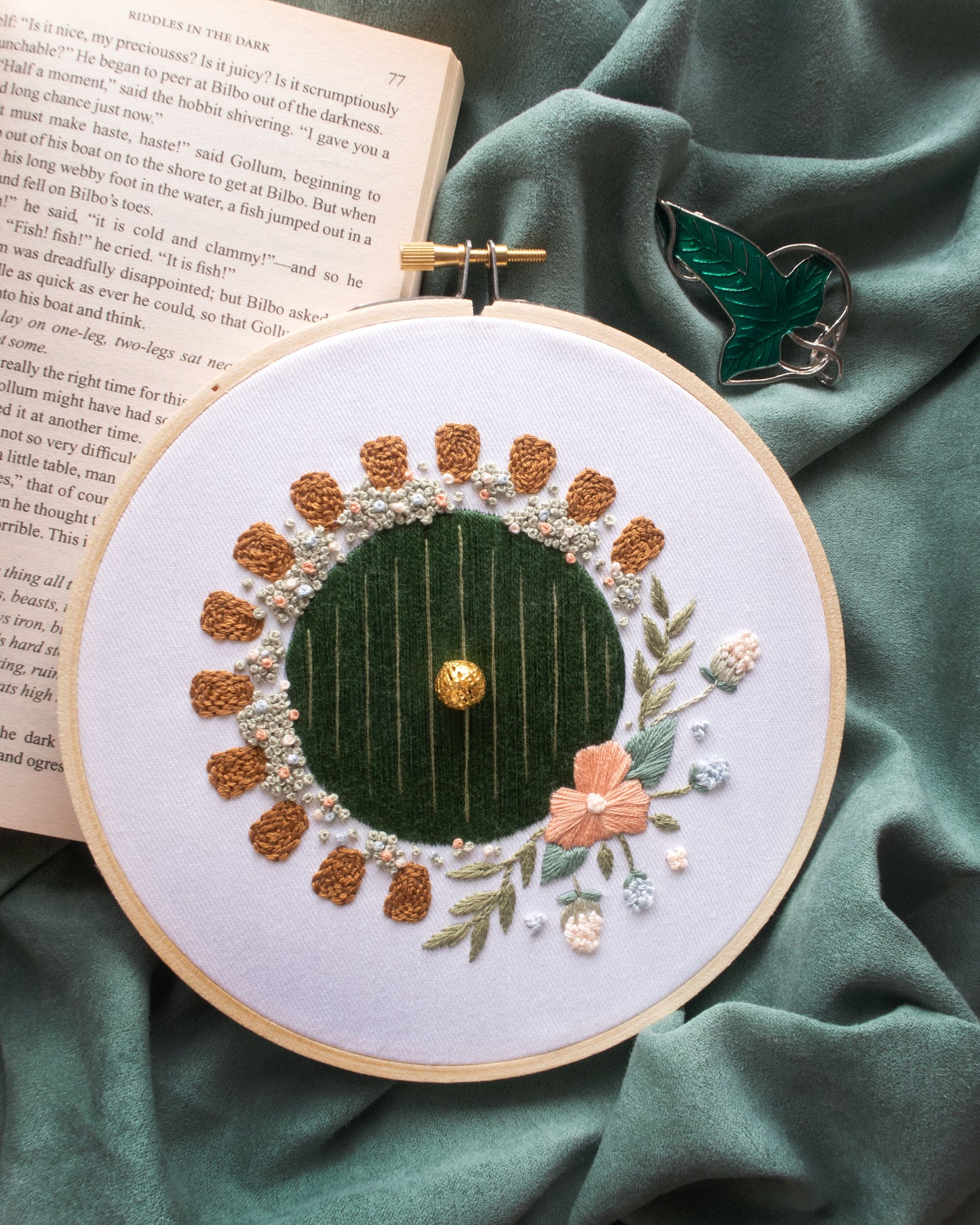 Hobbit Hole Embroidery Kit finished on green velvet background and green leaf cloak clasp and open book