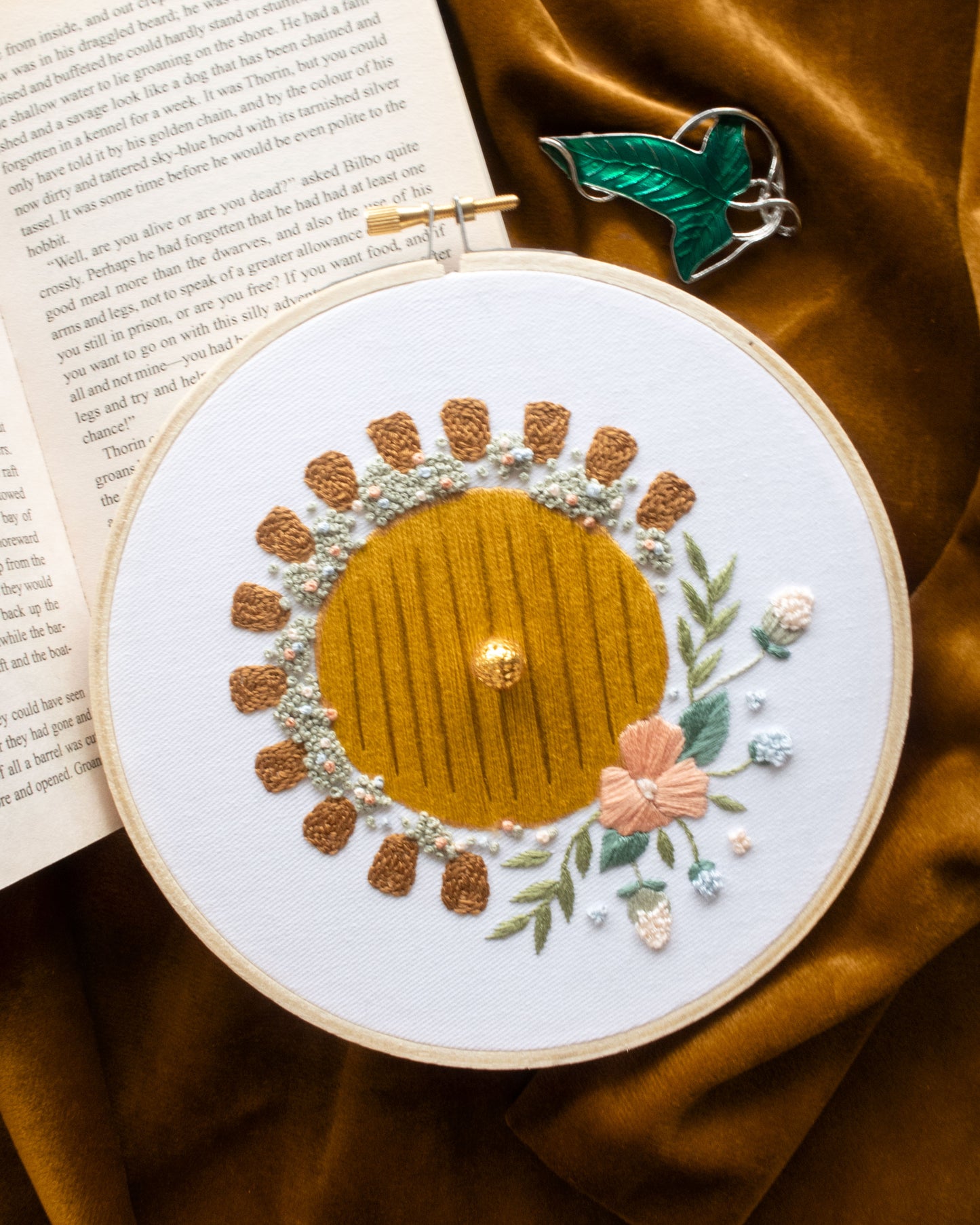 Hobbit Hole Embroidery Kit finished on dark yellow velvet background and green leaf cloak clasp and open book