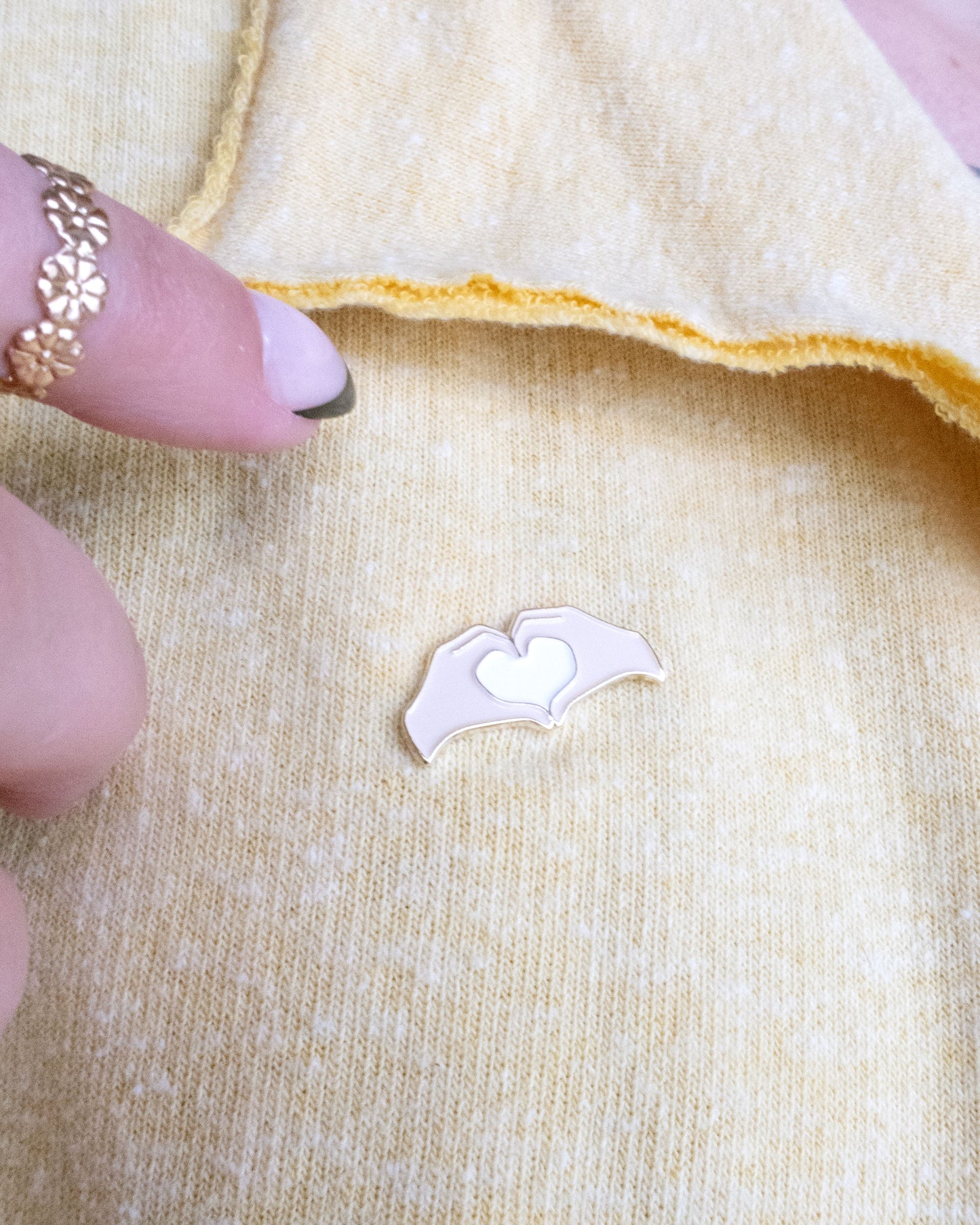 Heart Hands Embroidery Needle Minder on a yellow piece of fabric with hands