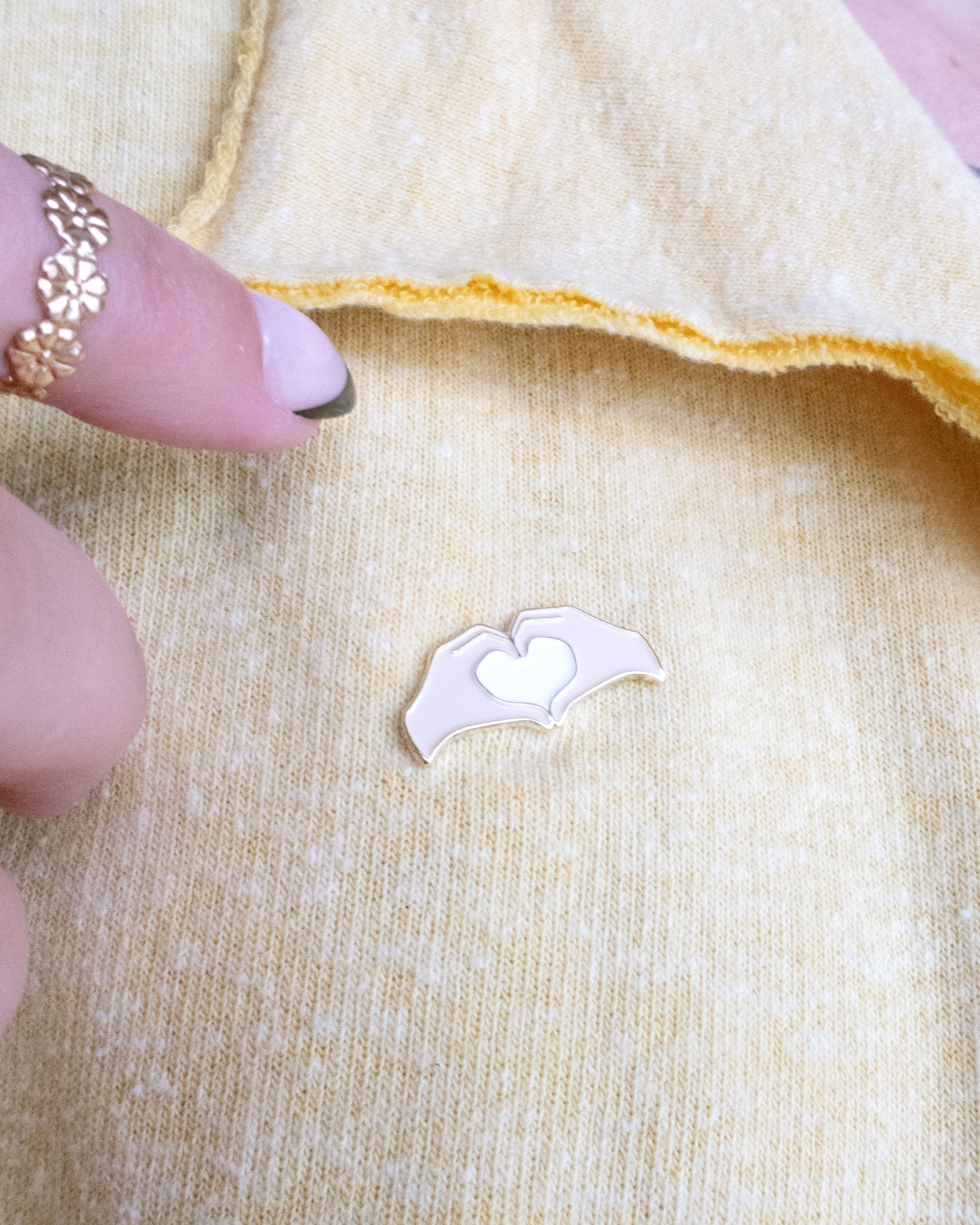 Heart Hands Embroidery Needle Minder on a yellow piece of fabric with hands