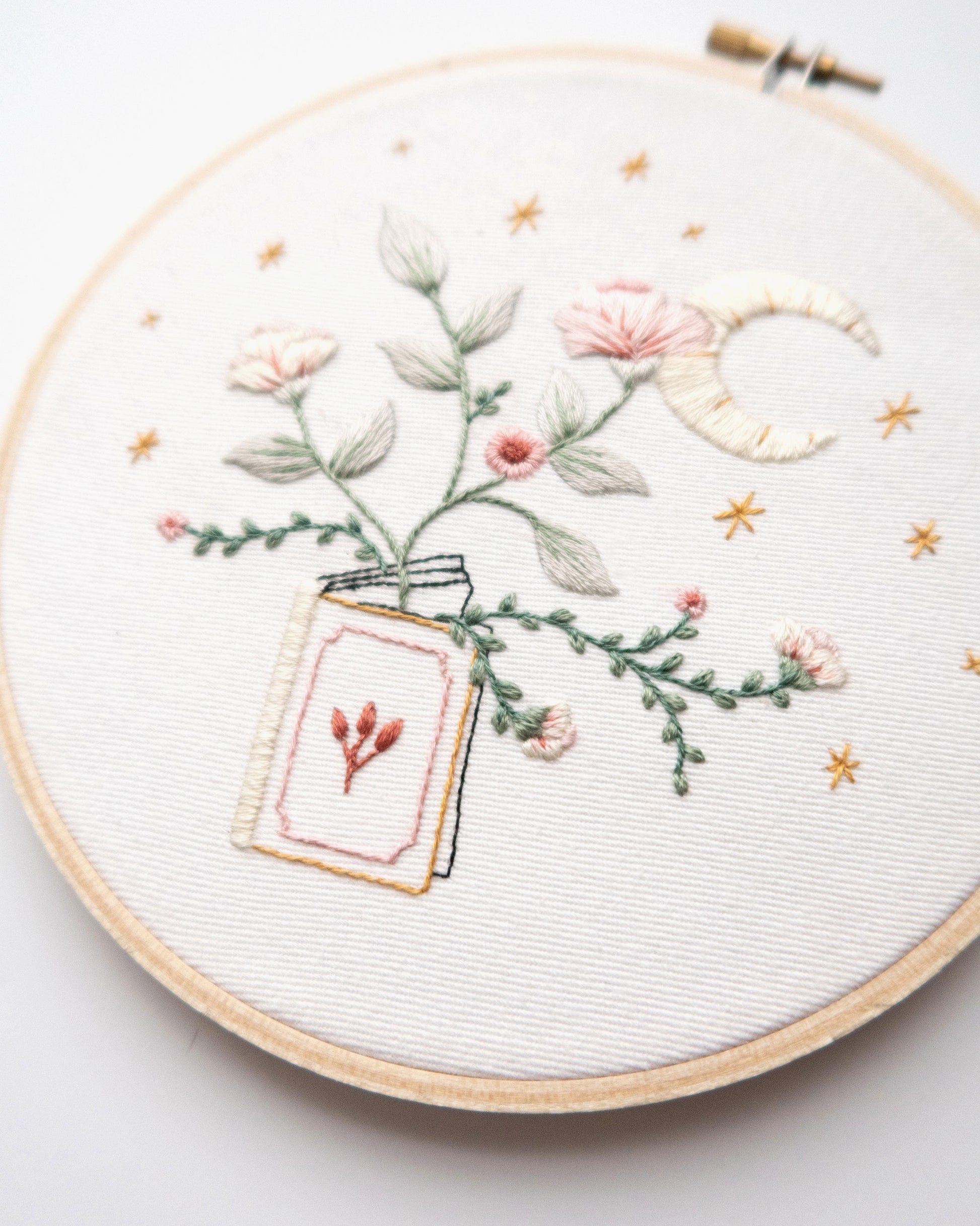 Embroidery pattern with open floral book with garden flowers and branches growing from open pages with stars and moon hand embroidery kit on embroidery hoop with boho dried florals close up finished