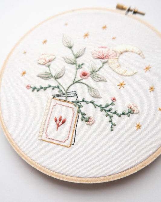Embroidery pattern with open floral book with garden flowers and branches growing from open pages with stars and moon hand embroidery kit on embroidery hoop with boho dried florals close up finished