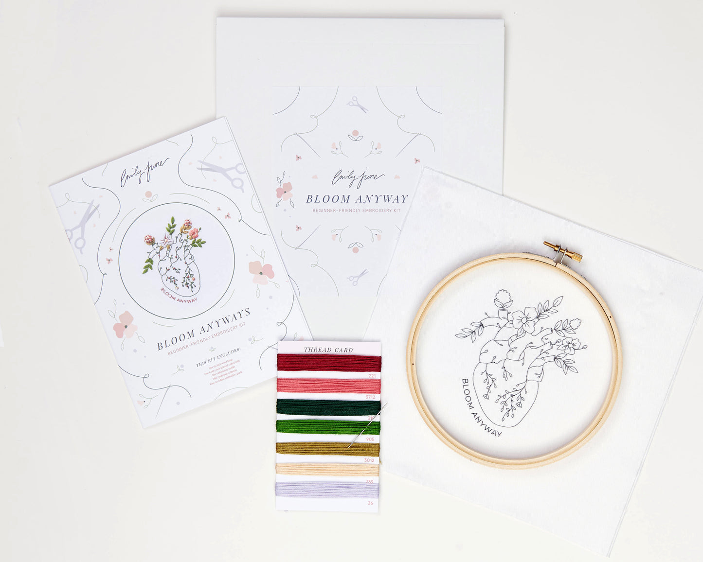 Bloom floral heart anatomy hand embroidery kit for mental health with pink, purple and red flowers and green leaves with DMC embroidery floss, printed embroidery fabric, embroidery needle, embroidery hoop and embroidery guide laid out on background