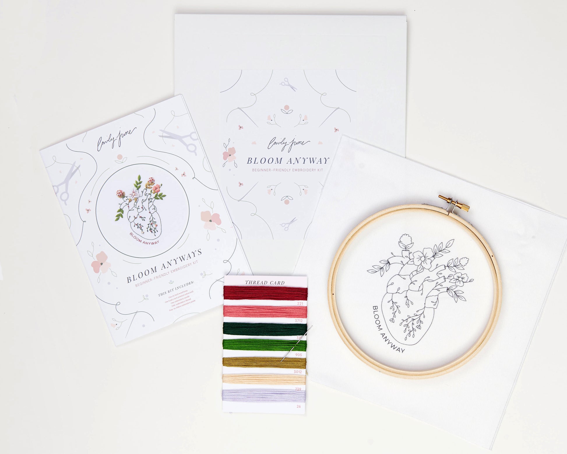 Bloom floral heart anatomy hand embroidery kit for mental health with pink, purple and red flowers and green leaves with DMC embroidery floss, printed embroidery fabric, embroidery needle, embroidery hoop and embroidery guide laid out on background