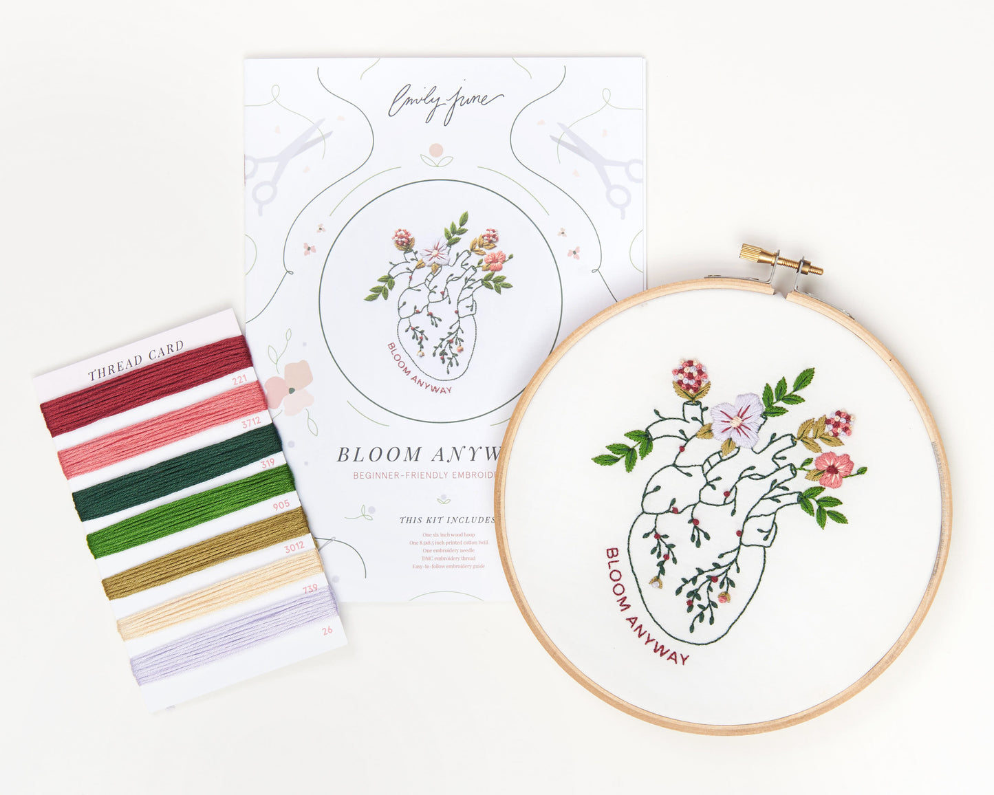 Bloom floral heart anatomy hand embroidery kit for mental health with pink, purple and red flowers and green leaves with DMC embroidery floss, printed embroidery fabric, embroidery needle, embroidery hoop and embroidery guide laid out in A shape