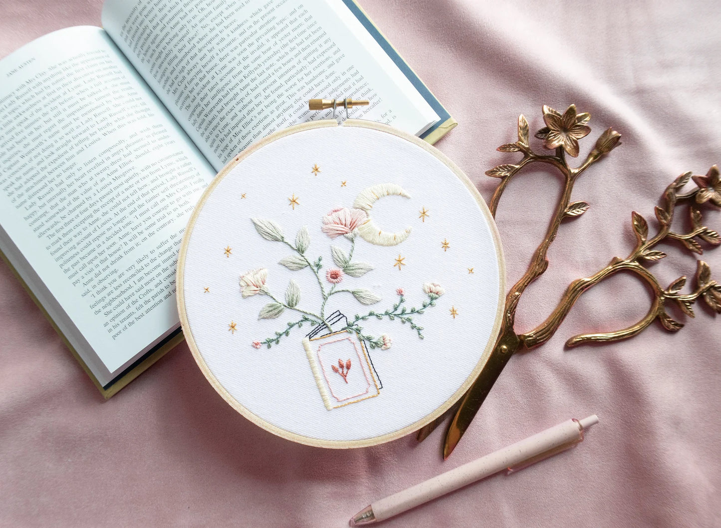 Embroidery pattern with open floral book with garden flowers and branches growing from open pages with stars and moon hand embroidery kit on embroidery hoop with boho dried florals on open book with floral scissors