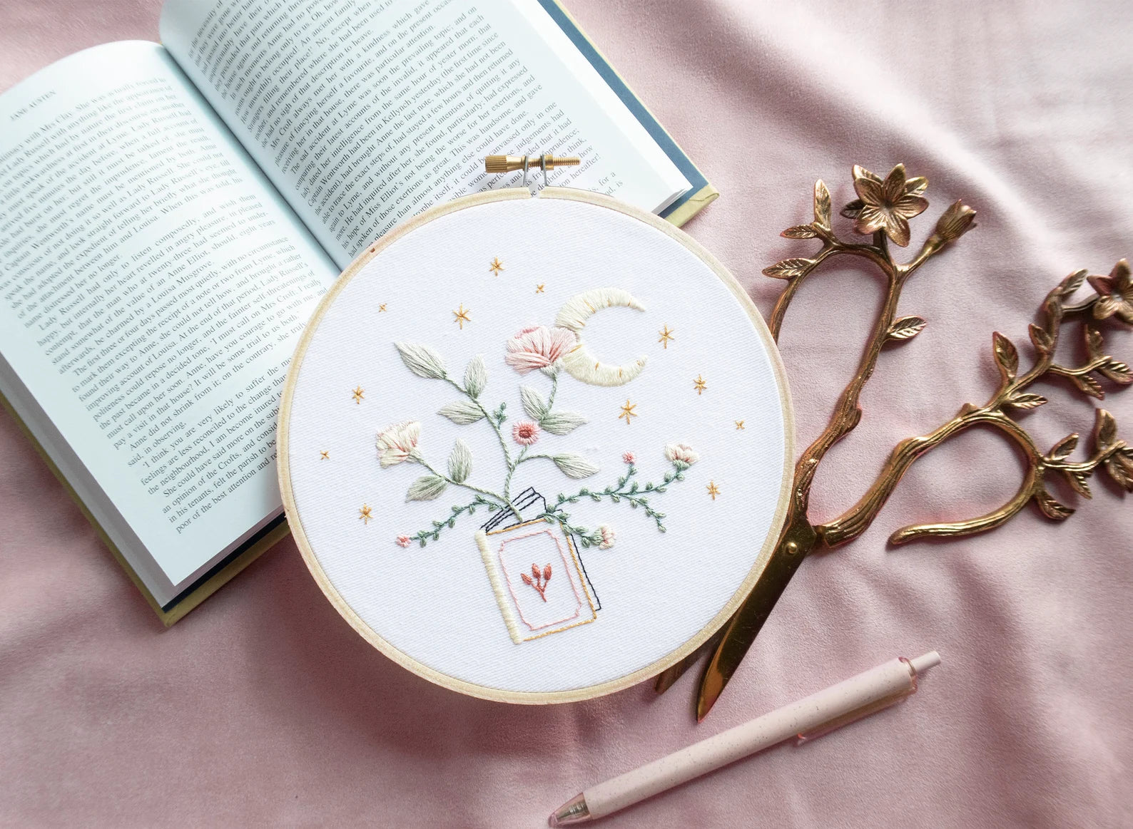 Embroidery pattern with open floral book with garden flowers and branches growing from open pages with stars and moon hand embroidery kit on embroidery hoop with boho dried florals on open book with floral scissors