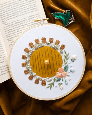 Hobbit Hole Embroidery Kit finished on dark yellow velvet background and green leaf cloak clasp and open book