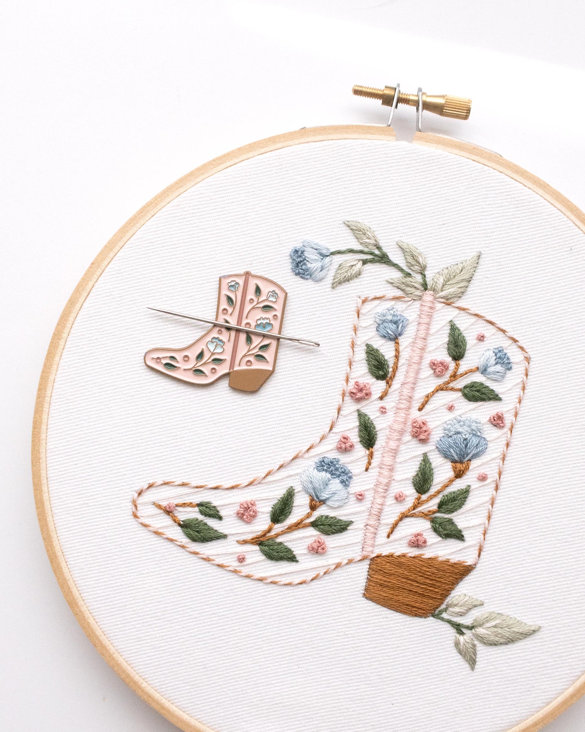 Floral cowboy boot hand embroidery kit with pink and blue flowers and light green leaves with pink cowboy boot needle minder or needle nanny 