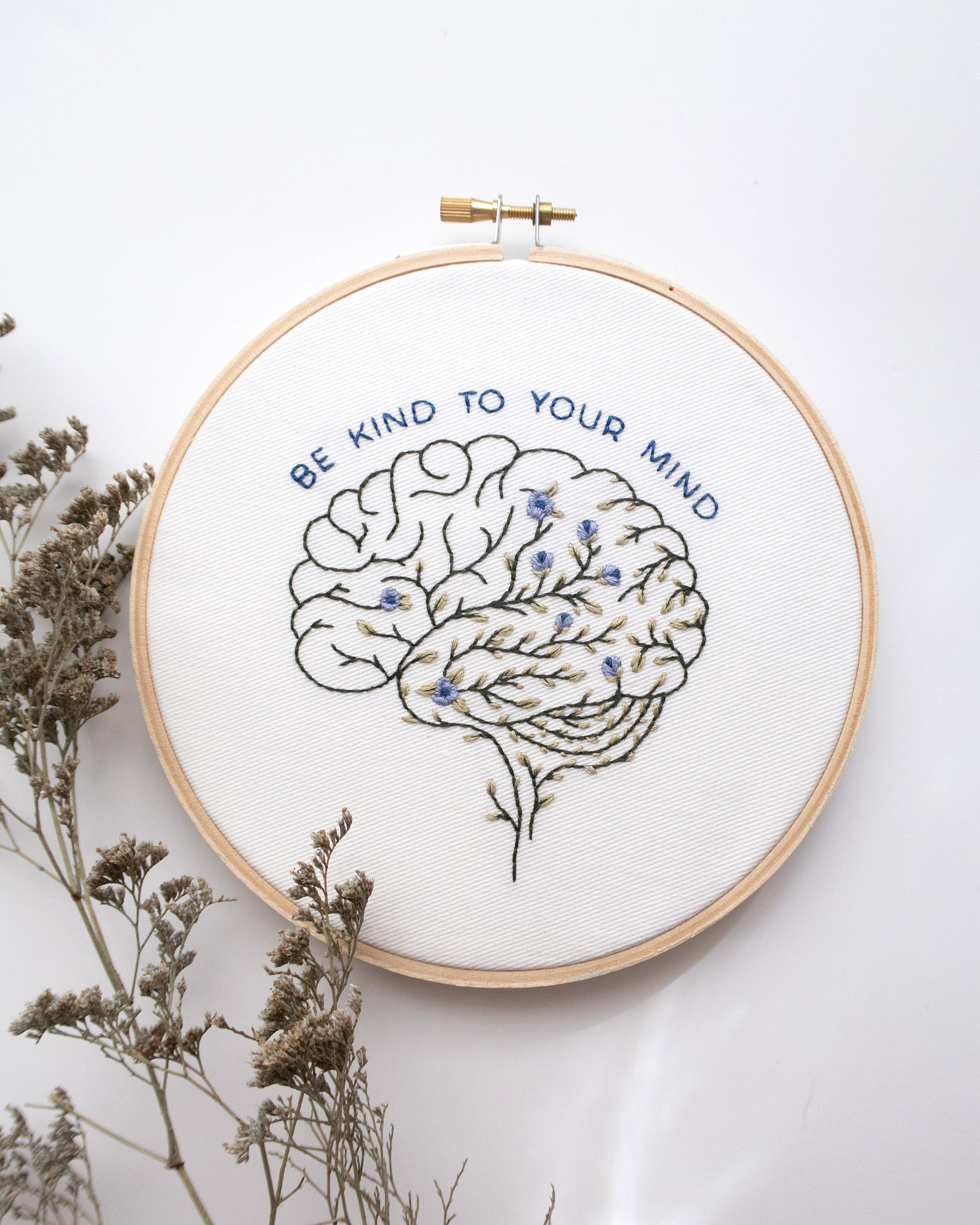 Floral anatomy hand embroidery pattern featuring floral brain with Be Kind to Your Mind mental health quote for mental health embroidery and beginner friendly embroidery on a white background with flowers