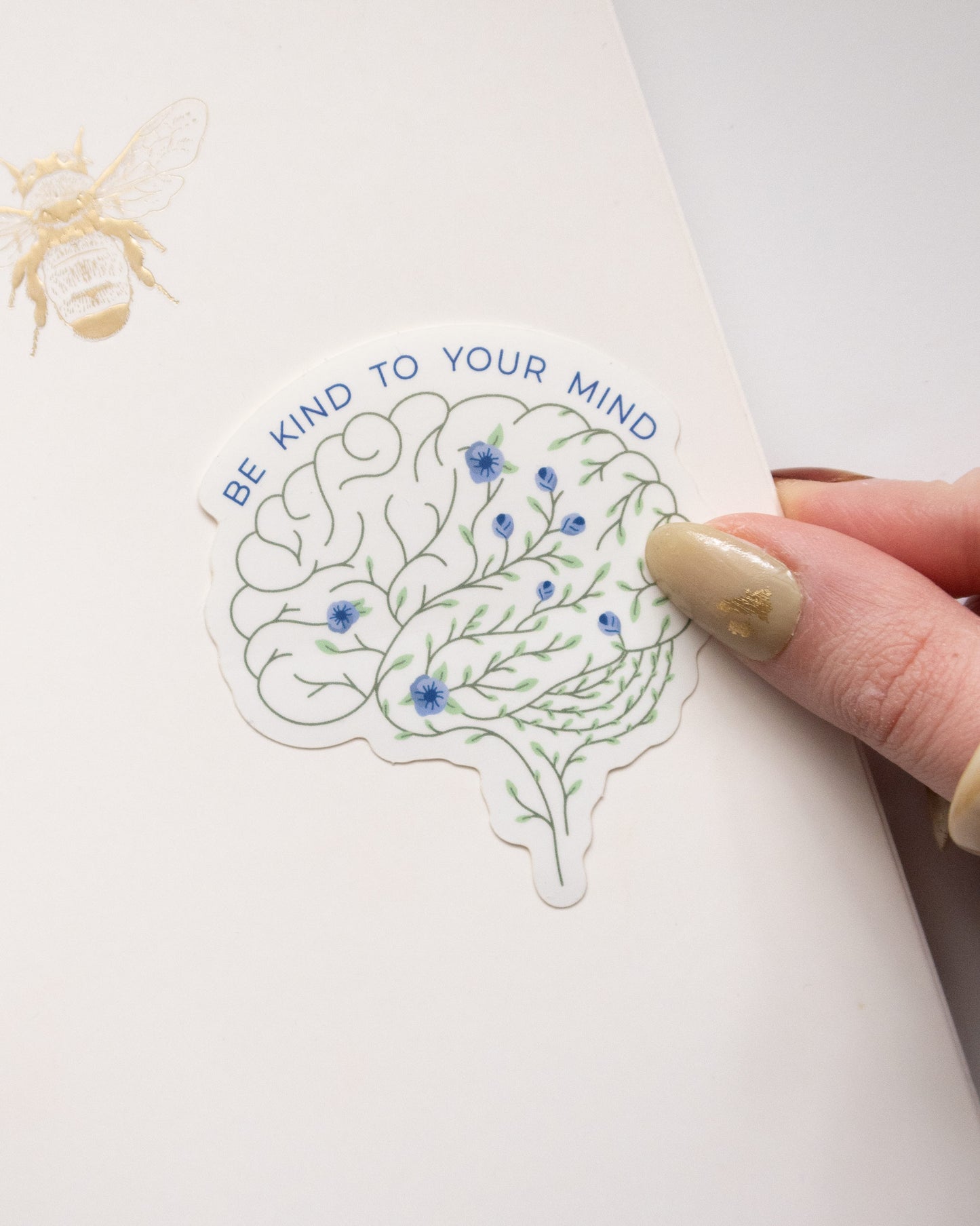 Be kind to your mind floral brain embroidery anatomy sticker, waterproof vinyl mental health sticker on surface with thumb pressing sticker down