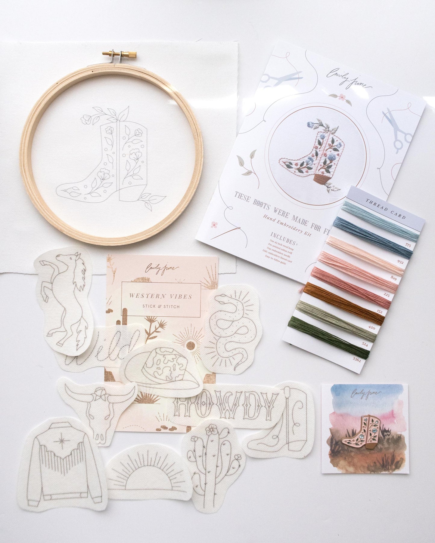 Southwest themed embroidery bundle with embroidery kit that includes wood embroidery hoop, printed embroidery fabric, embroidery needle, embroidery floss, and embroidery guide, and pink cowboy boot enamel needle nanny or needle minder, and western themed clothing embroidery stitch and stick pack with horse, wild in rope font, cow print cowboy hat, cowboy boot, howdy in western font, sunrise, western fringe jacket, boho floral skull, and boho snake design