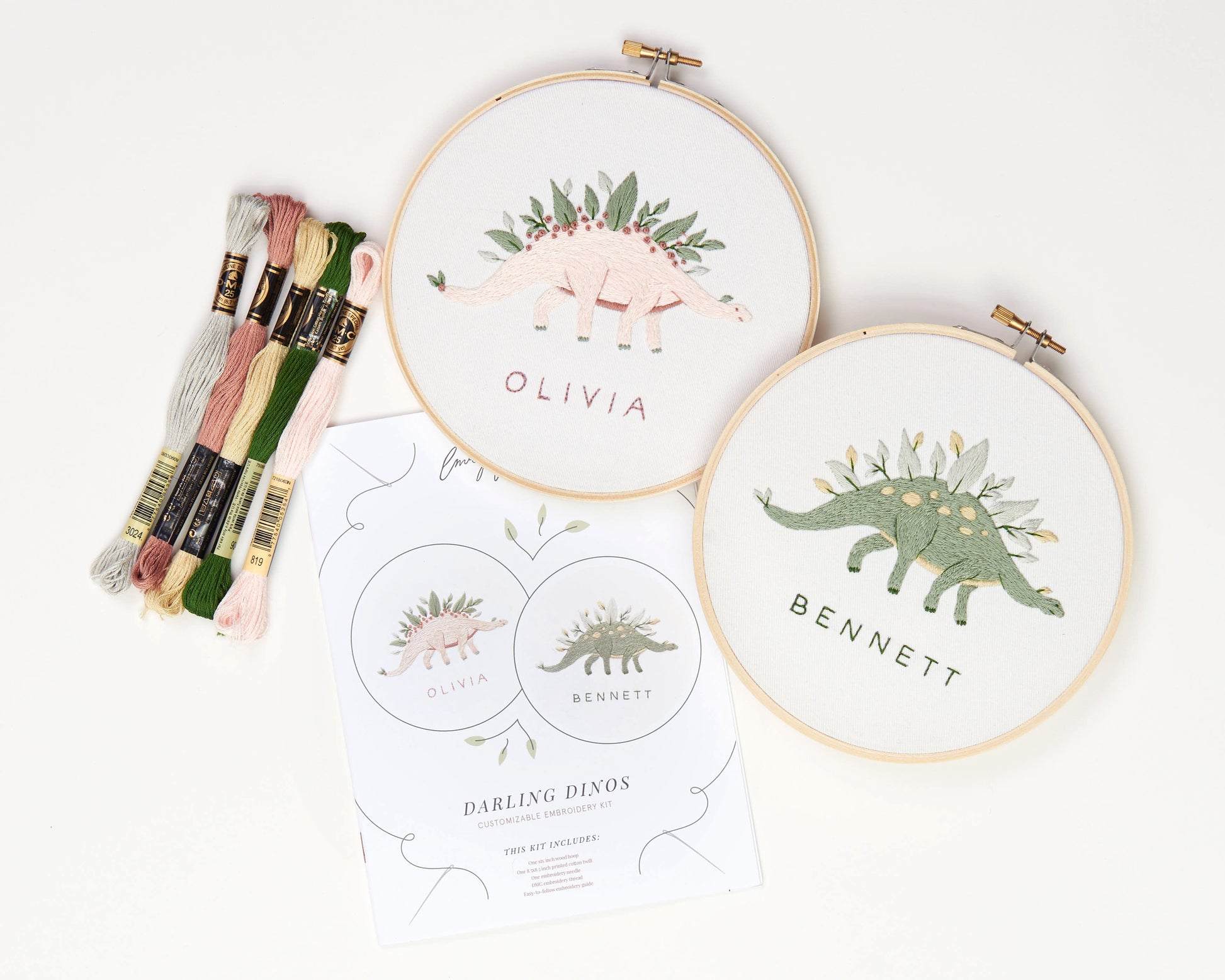 Green and pink dinosaur embroidery with leaves and flowers and custom baby name embroidery craft kit with heat erasable pen, embroidery floss in yellow pink and green, printed embroidery fabric, wood embroidery hoop and embroidery guide, close up contents