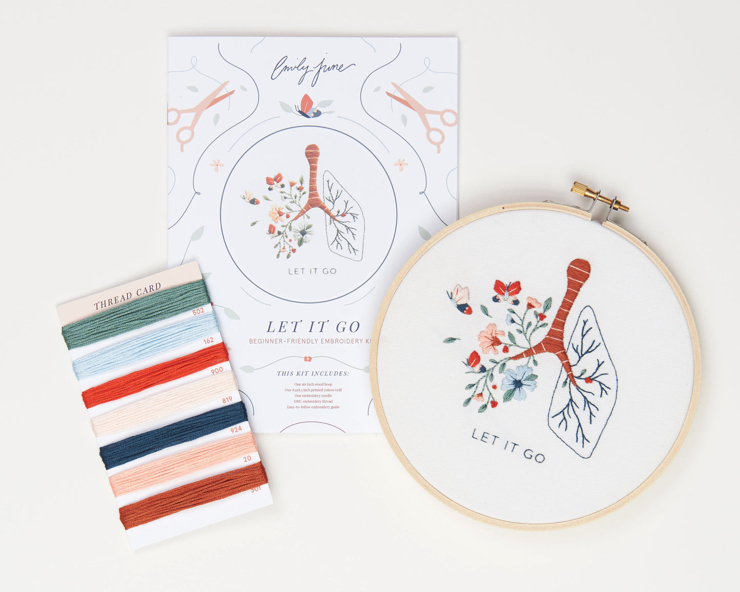 Let it go floral lung hand embroidery kit with pink and blue flowers and butterflies for mental health craft flat lay with printed embroidery fabric, wood embroidery hoop, embroidery guide, embroidery floss, and embroidery needle.